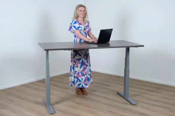 Vrouw staat achter een elektrisch bureau met een aluminium poot en een donker eiken blad.